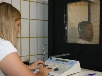Ilustrasi pemeriksa mengoperasikan audiometer saat pria dewasa berpenyuara telinga duduk di bilik kedap suara