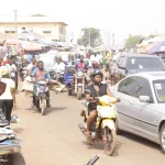 Pengendara sepeda motor memadati jalan pasar di antara mobil dan pedagang di Tamale, Ghana