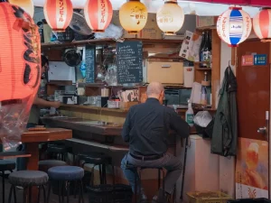Ilustrasi seorang lelaki duduk membelakangi kamera di kedai izakaya berlampion di Tokyo