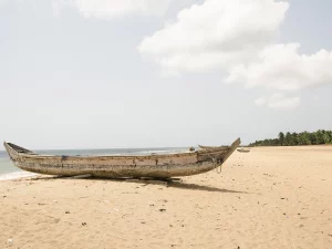 Ilustrasi perahu kano kayu tertambat di pasir Pantai Tegbi, Volta Region, Ghana