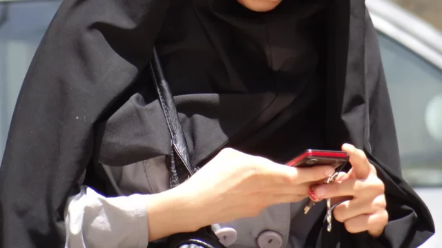 Ilustrasi tangan perempuan memegang ponsel merah di tepi jalan Kermanshah, Iran