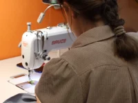 Seorang perempuan berkepang menjahit kain dengan mesin jahit industri