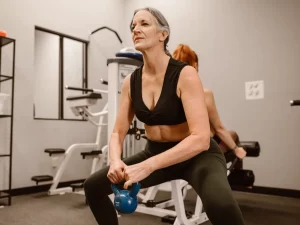Ilustrasi perempuan paruh baya melakukan squat sambil memegang kettlebell biru di ruang kebugaran