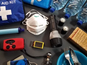 Ilustrasi isi tas siaga bencana: kotak P3K, senter, radio, dan air minum