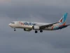 Pesawat Flydubai terbang dengan roda pendarat terbuka di bawah langit mendung