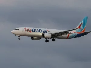 Pesawat Flydubai terbang dengan roda pendarat terbuka di bawah langit mendung