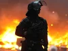 Polisi antihuru-hara berhelm dan bersenjata berdiri di depan api barikade yang menyala