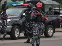 Polisi Nigeria bersenjata dan berhelm berjaga di samping mobil patroli polisi