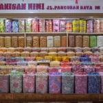 Ilustrasi rak toko jajanan di Jakarta penuh toples permen dan manisan warna-warni