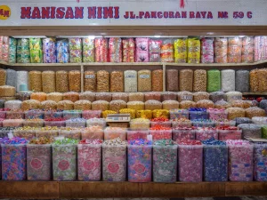 Ilustrasi rak toko jajanan di Jakarta penuh toples permen dan manisan warna-warni