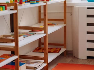 Ilustrasi rak kayu berisi mainan edukatif dan papan puzzle di ruang kelas anak usia dini