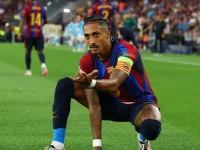 Raphinha berban kapten berlutut di lapangan dengan seragam biru merah Barcelona