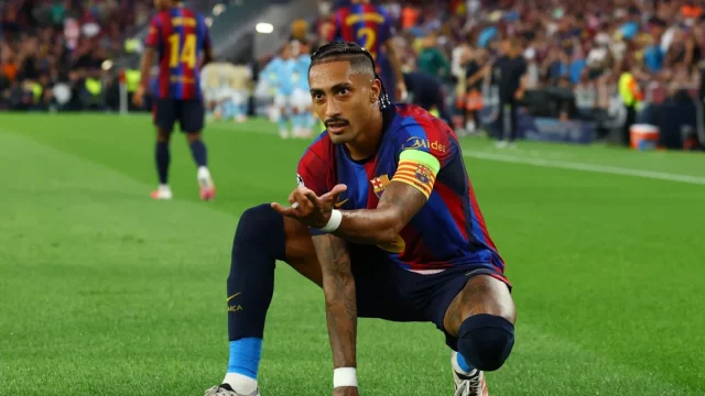 Raphinha berban kapten berlutut di lapangan dengan seragam biru merah Barcelona