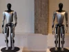Dua robot humanoid Tesla Optimus berwarna perak dan hitam dipajang di atas alas bundar
