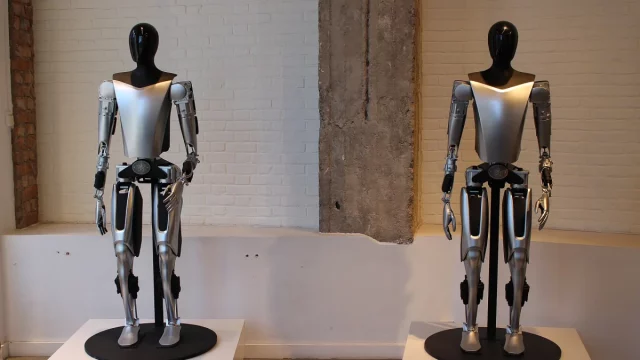 Dua robot humanoid Tesla Optimus berwarna perak dan hitam dipajang di atas alas bundar
