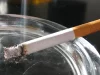 Ilustrasi sebatang rokok menyala bersandar di tepi asbak kaca dengan abu dan asap tipis