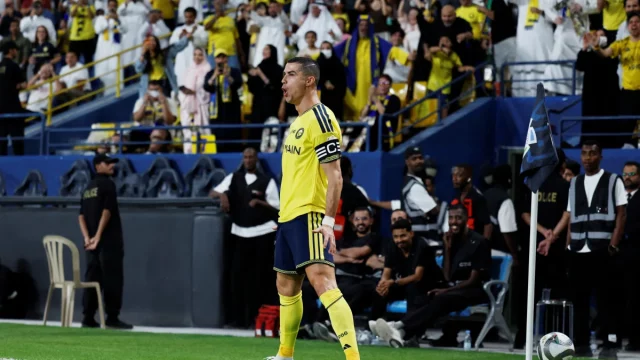 Cristiano Ronaldo berseragam kuning Al Nassr berdiri di lapangan dengan tribune penonton di belakangnya