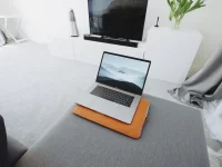 Ilustrasi ruang keluarga serba putih dengan sofa abu-abu, televisi, dan laptop terbuka