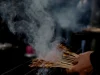 Tusuk sate berjajar di atas bara panggangan dengan asap mengepul di kedai jalanan