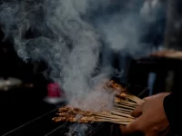 Tusuk sate berjajar di atas bara panggangan dengan asap mengepul di kedai jalanan