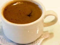 Ilustrasi: secangkir kopi Turki berbusa dalam cangkir putih di atas tatakan beralas kertas renda