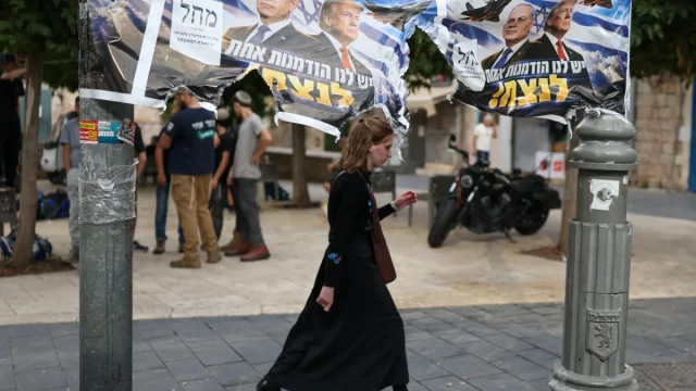Seorang perempuan berjalan melewati spanduk kampanye bergambar Benjamin Netanyahu dan Donald Trump