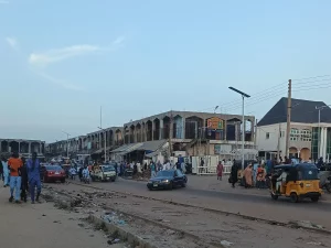 Ilustrasi jalan di kawasan pasar kota Sokoto, Nigeria, dengan deretan ruko dan becak motor kuning