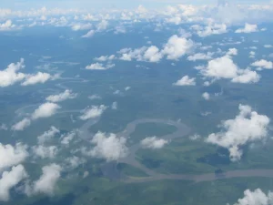 Ilustrasi sungai berkelok di dataran rendah hijau Merauke di bawah awan, tampak dari udara