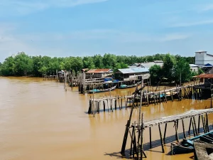 Ilustrasi rumah panggung, titian kayu, dan perahu nelayan di tepi Sungai Parit V, Kuala Tungkal, Jambi