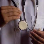 Ilustrasi dua tangan seseorang berjas putih dokter menggenggam stetoskop di depan dada