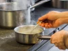 Ilustrasi tangan juru masak mengaduk saus di panci baja yang mengepul di dapur restoran