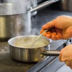 Ilustrasi tangan juru masak mengaduk saus di panci baja yang mengepul di dapur restoran