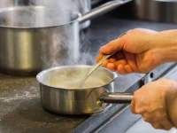 Ilustrasi tangan juru masak mengaduk saus di panci baja yang mengepul di dapur restoran