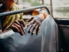 Ilustrasi tangan keriput seorang perempuan lanjut usia bertumpu pada sandaran kursi bus