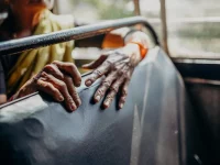 Ilustrasi tangan keriput seorang perempuan lanjut usia bertumpu pada sandaran kursi bus