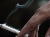 Ilustrasi tangan memegang sebatang rokok menyala dengan asap tipis mengepul