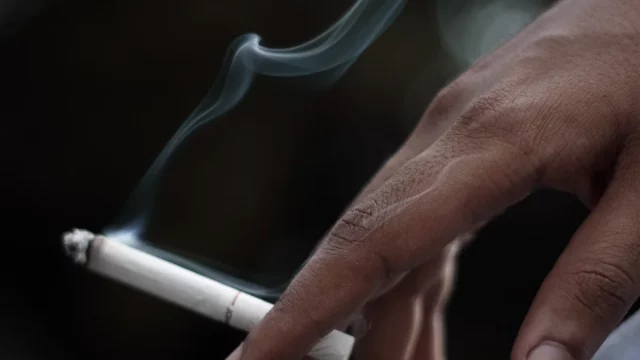 Ilustrasi tangan memegang sebatang rokok menyala dengan asap tipis mengepul