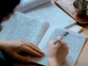 Ilustrasi tangan menulis aksara Asia Timur dengan pena di buku tulis berkotak
