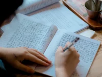 Ilustrasi tangan menulis aksara Asia Timur dengan pena di buku tulis berkotak