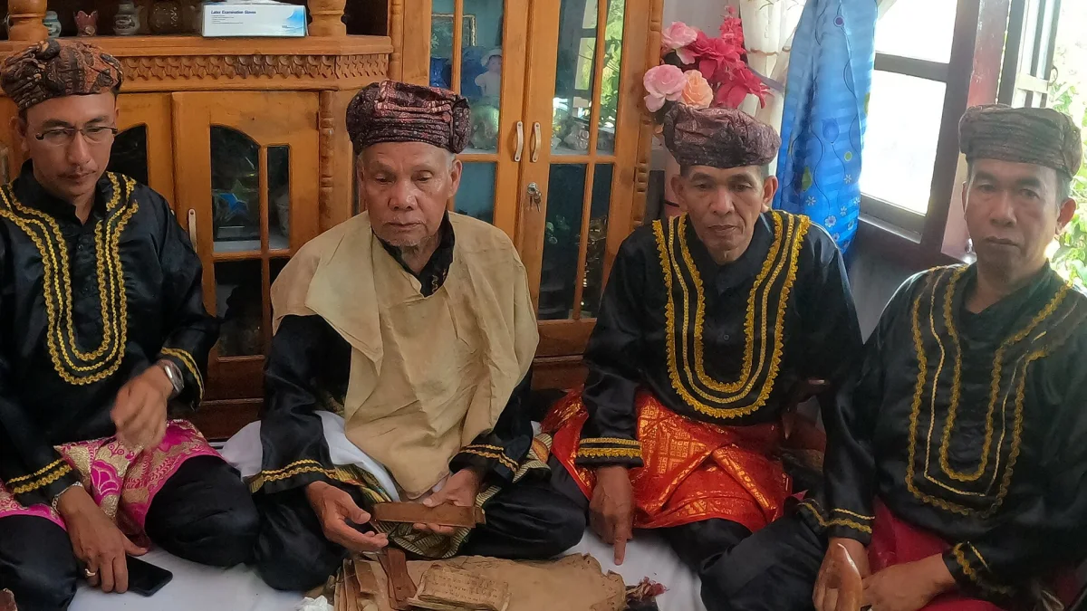 Empat tetua adat berbaju hitam bersulam emas duduk bersila saat Kenduri Sko