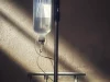 Ilustrasi botol cairan infus tergantung di tiang dalam kamar rawat yang temaram