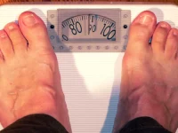 Ilustrasi sepasang kaki telanjang berdiri di atas timbangan badan analog berwarna putih