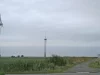 Tiga turbin angin di padang rumput Windpark Pilsum, Krummhörn, Jerman utara, di bawah langit mendung