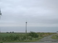 Tiga turbin angin di padang rumput Windpark Pilsum, Krummhörn, Jerman utara, di bawah langit mendung