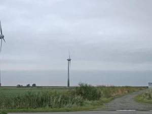 Tiga turbin angin di padang rumput Windpark Pilsum, Krummhörn, Jerman utara, di bawah langit mendung