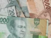 Uang kertas rupiah pecahan dua puluh ribu dan lima puluh ribu tergeletak di atas meja kayu