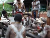 Ilustrasi sekelompok laki-laki Asmat berhias cat tubuh putih berjongkok mengelilingi batang kayu di Papua