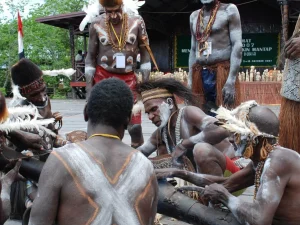 Ilustrasi sekelompok laki-laki Asmat berhias cat tubuh putih berjongkok mengelilingi batang kayu di Papua