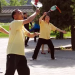 Tiga lansia berkaus kuning bermain bola raket tai chi di Taman Tiantan, Beijing, Tiongkok