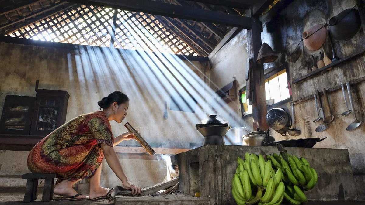 Perempuan Osing meniup api tungku dengan semprong bambu di Desa Kemiren, Banyuwangi